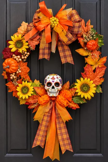 Corona para puerta con moños de listón naranja, girasoles y calavera
